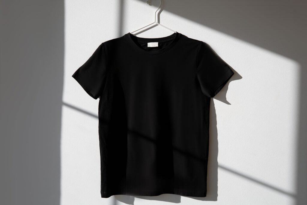 Black t-shirt hanging on a hanger against a white wall